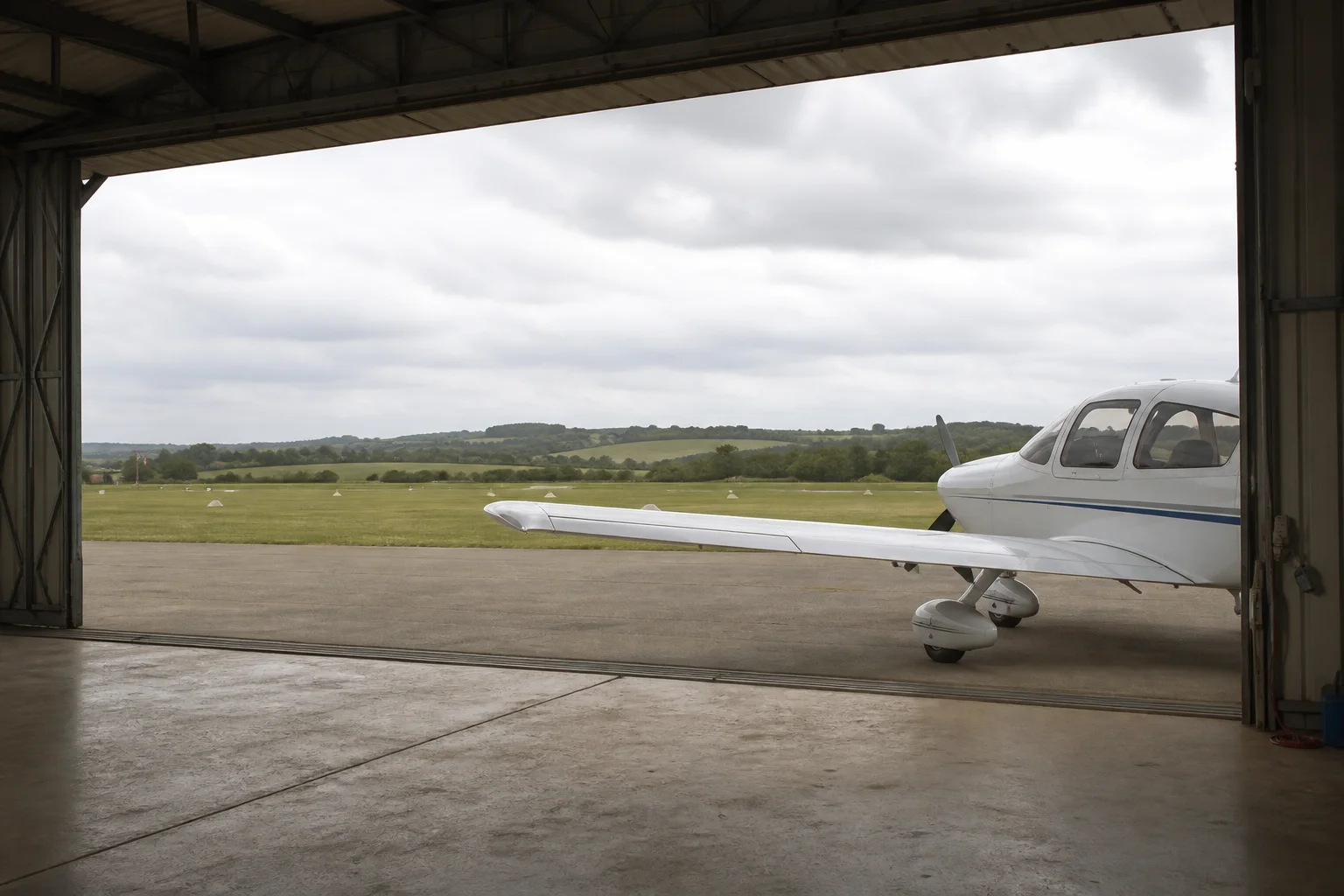 Un avion léger devant un hangar ouvert sur un terrain en herbe